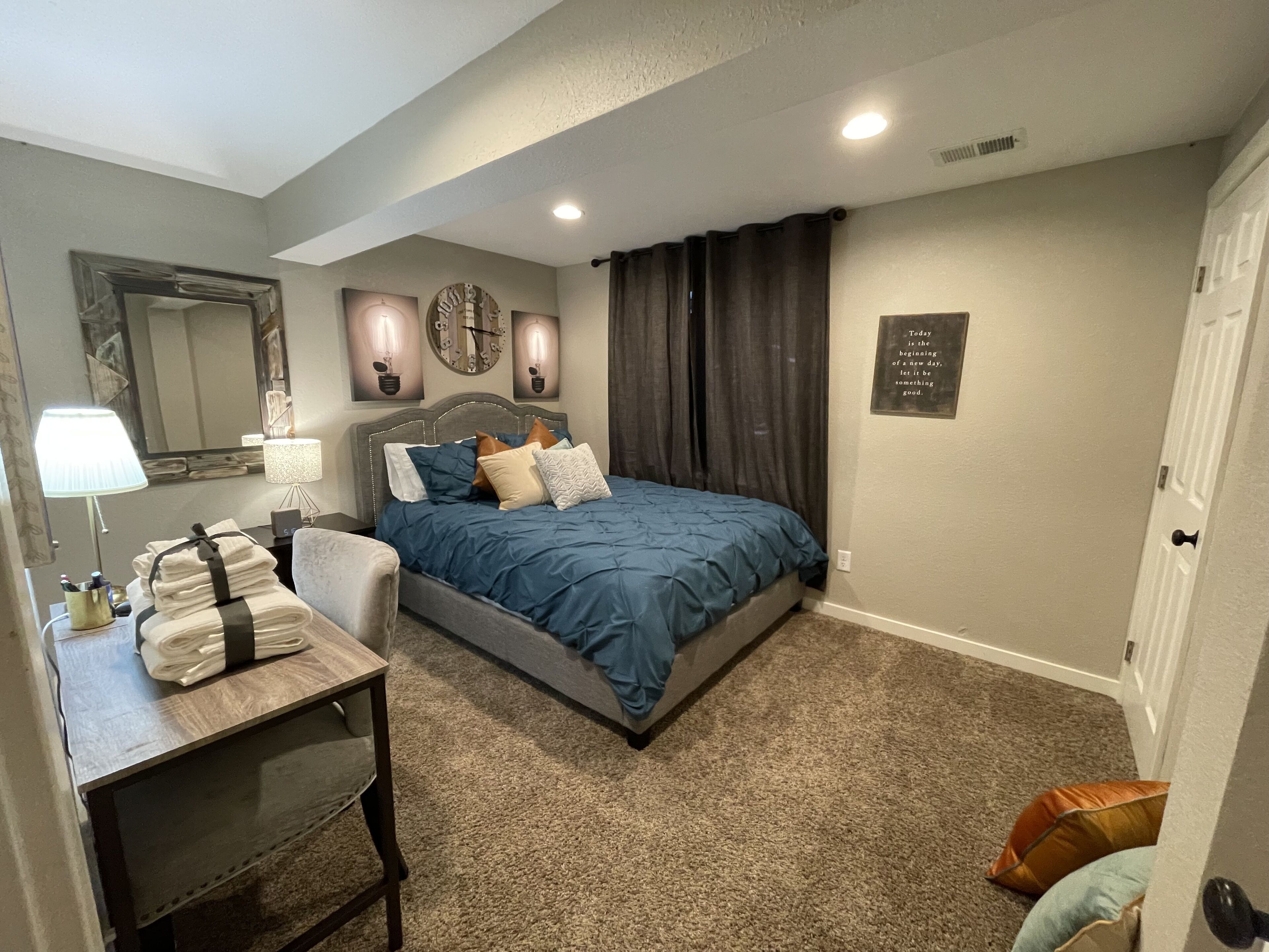 Un dormitorio con cama, escritorio, lámpara, espejo y un reloj de pared.
