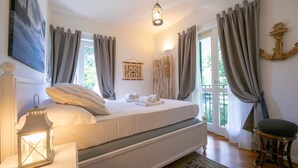 Ein Schlafzimmer mit Bett, einer Pendelleuchte, einem Sessel und Blick ins Freie.