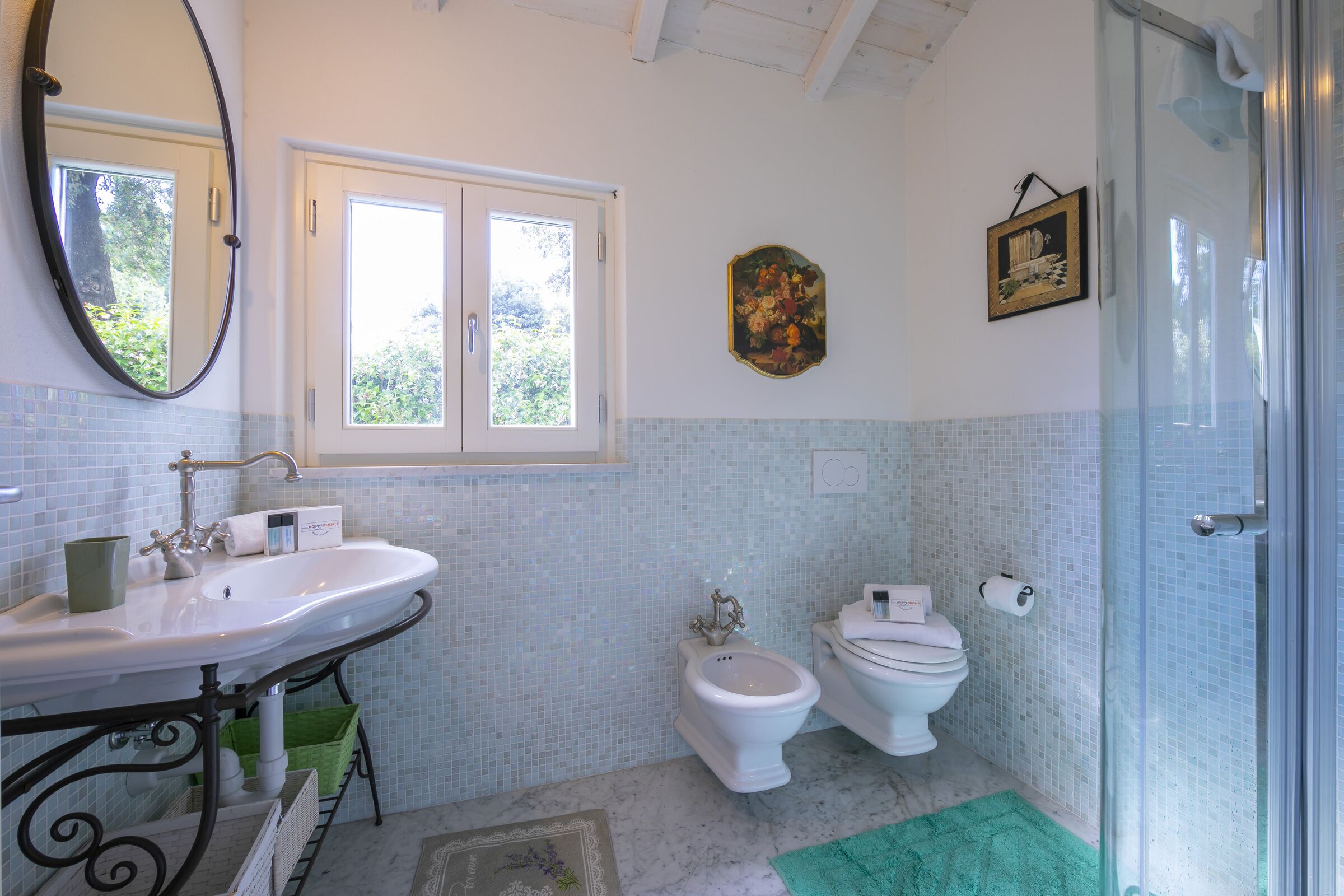Une salle de bain avec un lavabo blanc, deux toilettes, un miroir et une fenêtre.
