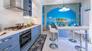 Eine moderne Küche mit Gasherd, Backofen und blauen Schränken. Es gibt eine Essecke mit einem weißen Tisch und blauen Stühlen.