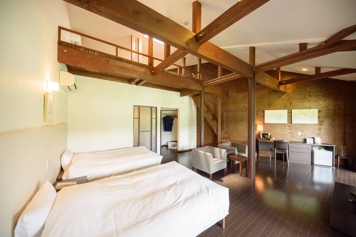 A room with two beds, a desk, and a staircase leading to an upper level.