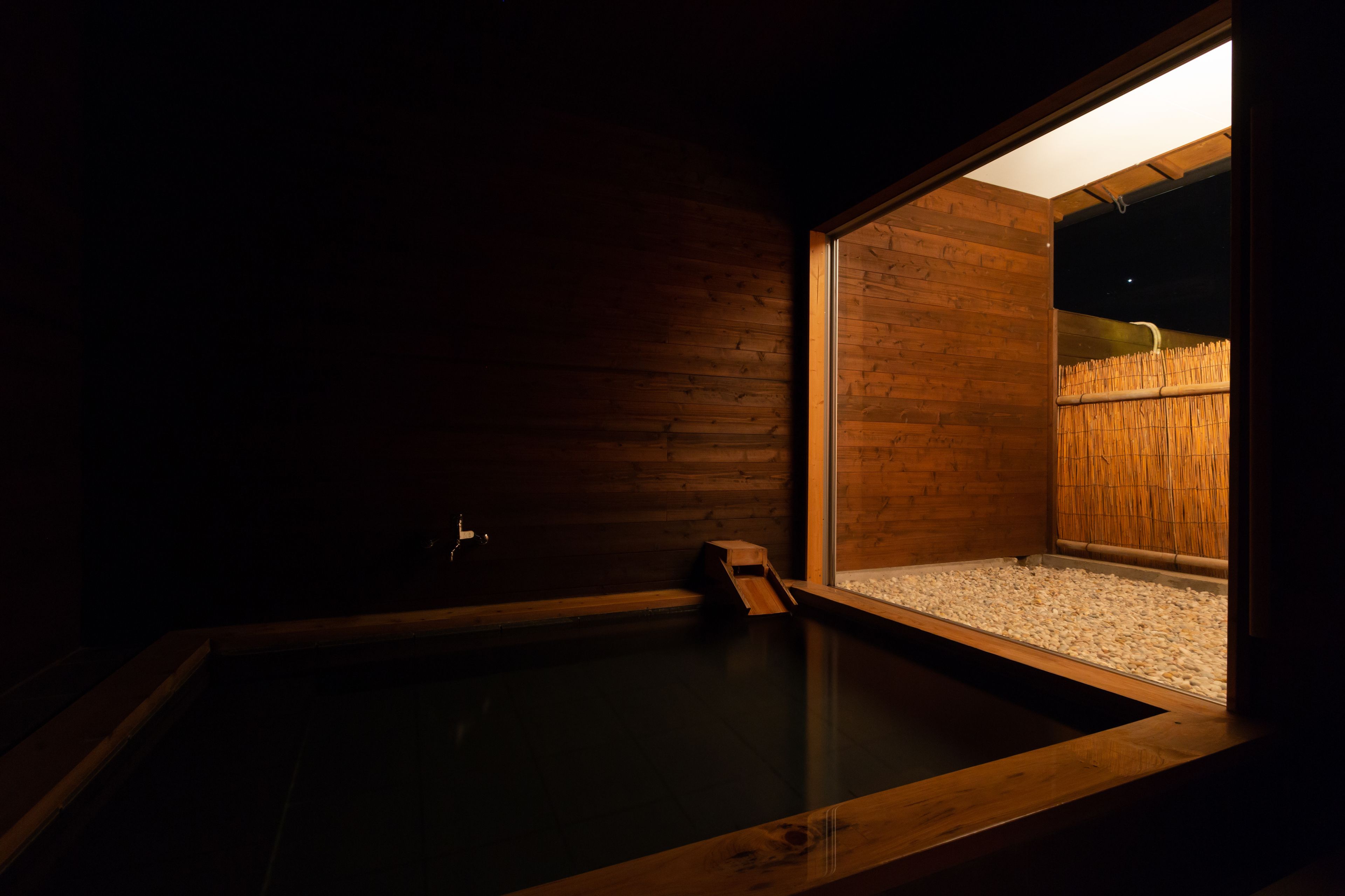 A wooden room with a hot tub, a window, and a bamboo fence visible through the window.