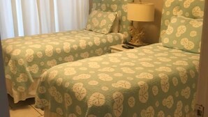 Una stanza con due letti, ognuno con una coperta e cuscini a motivi floreali verdi. Tra i letti, un comodino con una lampada.