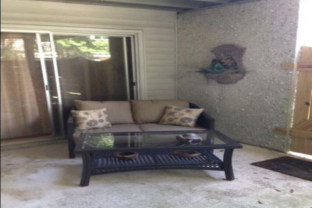 A room with a sliding glass door, a beige sofa with patterned cushions, and a glass coffee table.