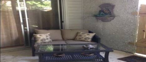 A room with a sliding glass door, a beige sofa with patterned cushions, and a glass coffee table.