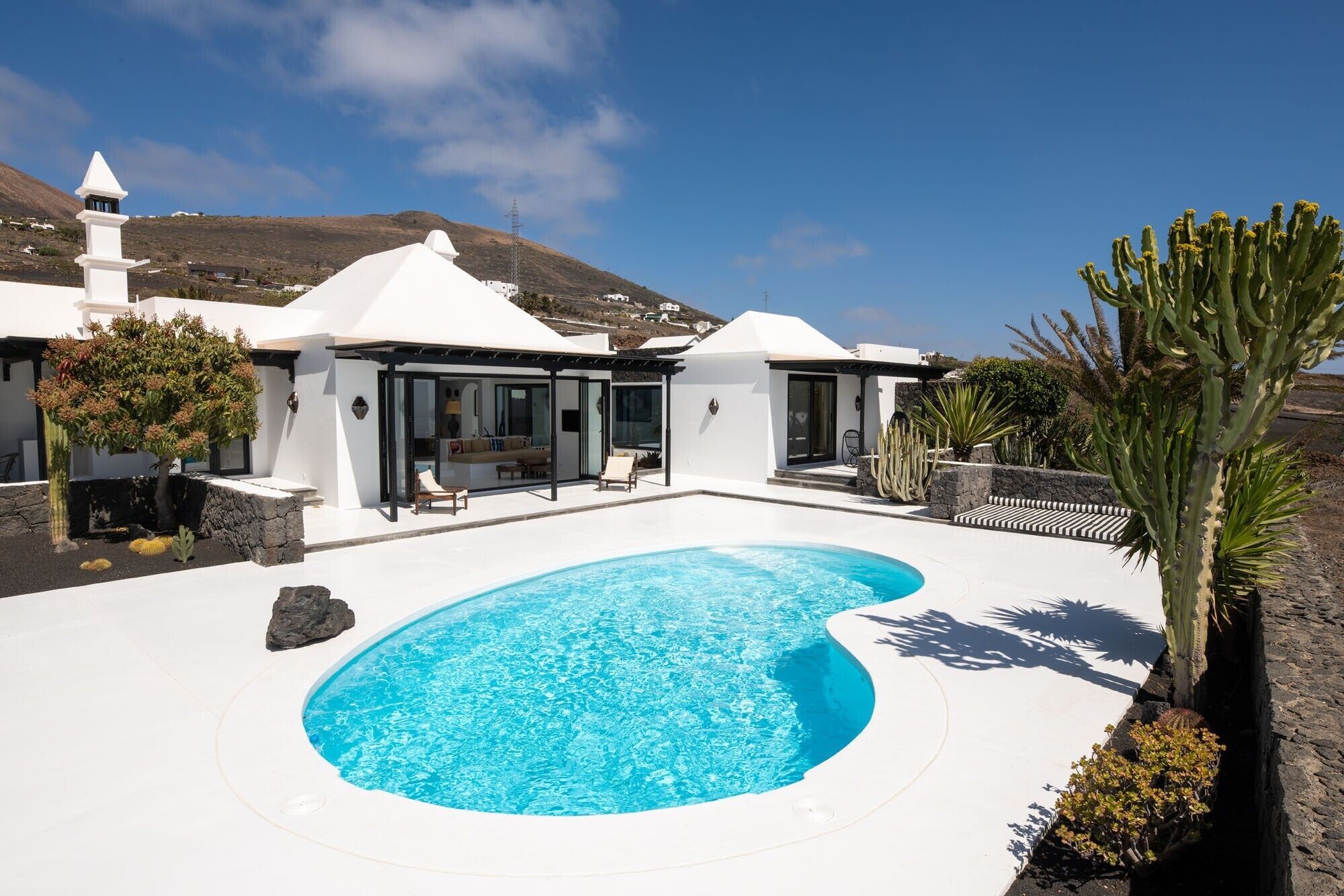 A modern villa with a swimming pool, outdoor seating, and a view of a mountainous landscape.