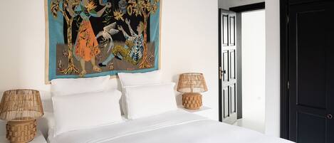 A bed with white linens, a large abstract painting above it, and two wicker lamps on either side.