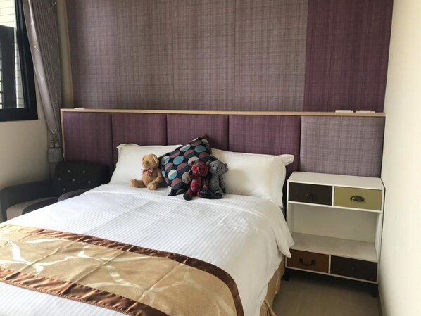 Una cama bien hecha con una colcha estampada, una mesita de noche con cajones y un amplio ventanal con cortinas.