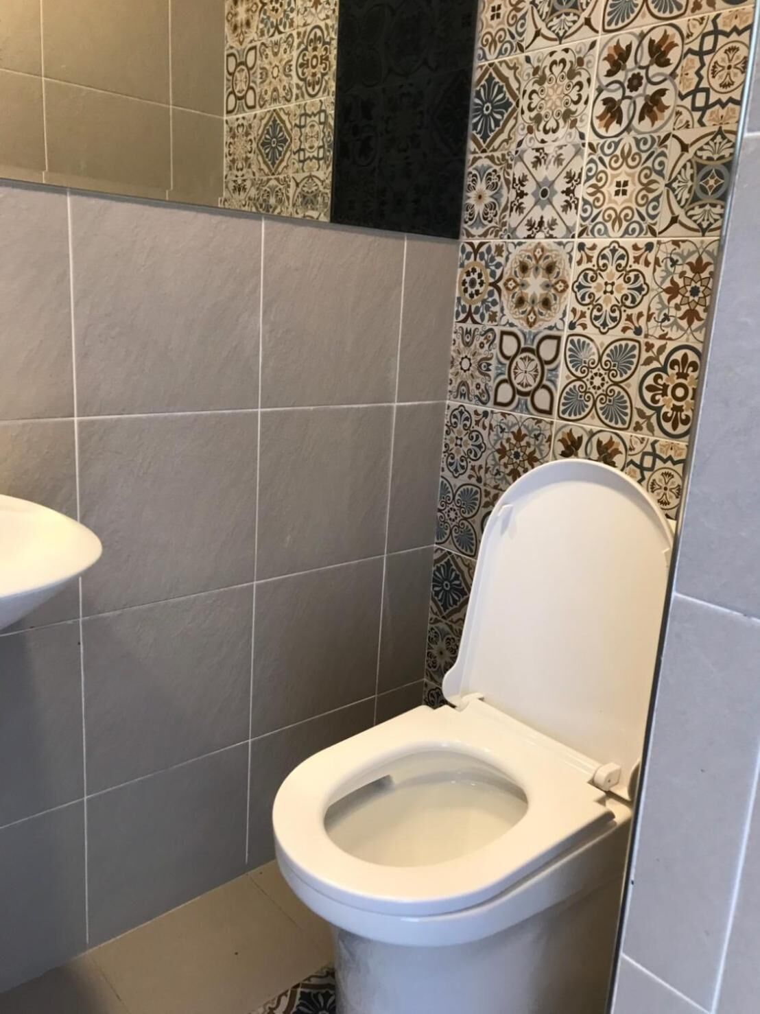 A small bathroom with a toilet, a sink, and patterned tiles on the walls.