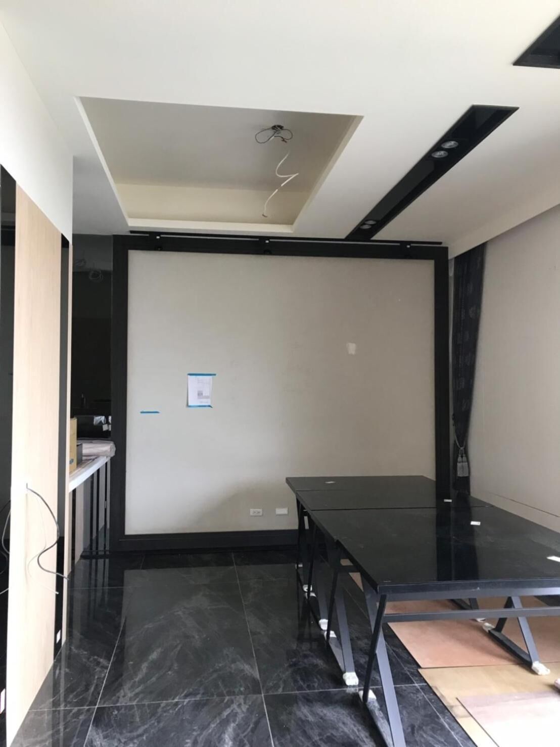A modern, minimalist room with a black table, a ceiling light fixture, and a tiled floor.