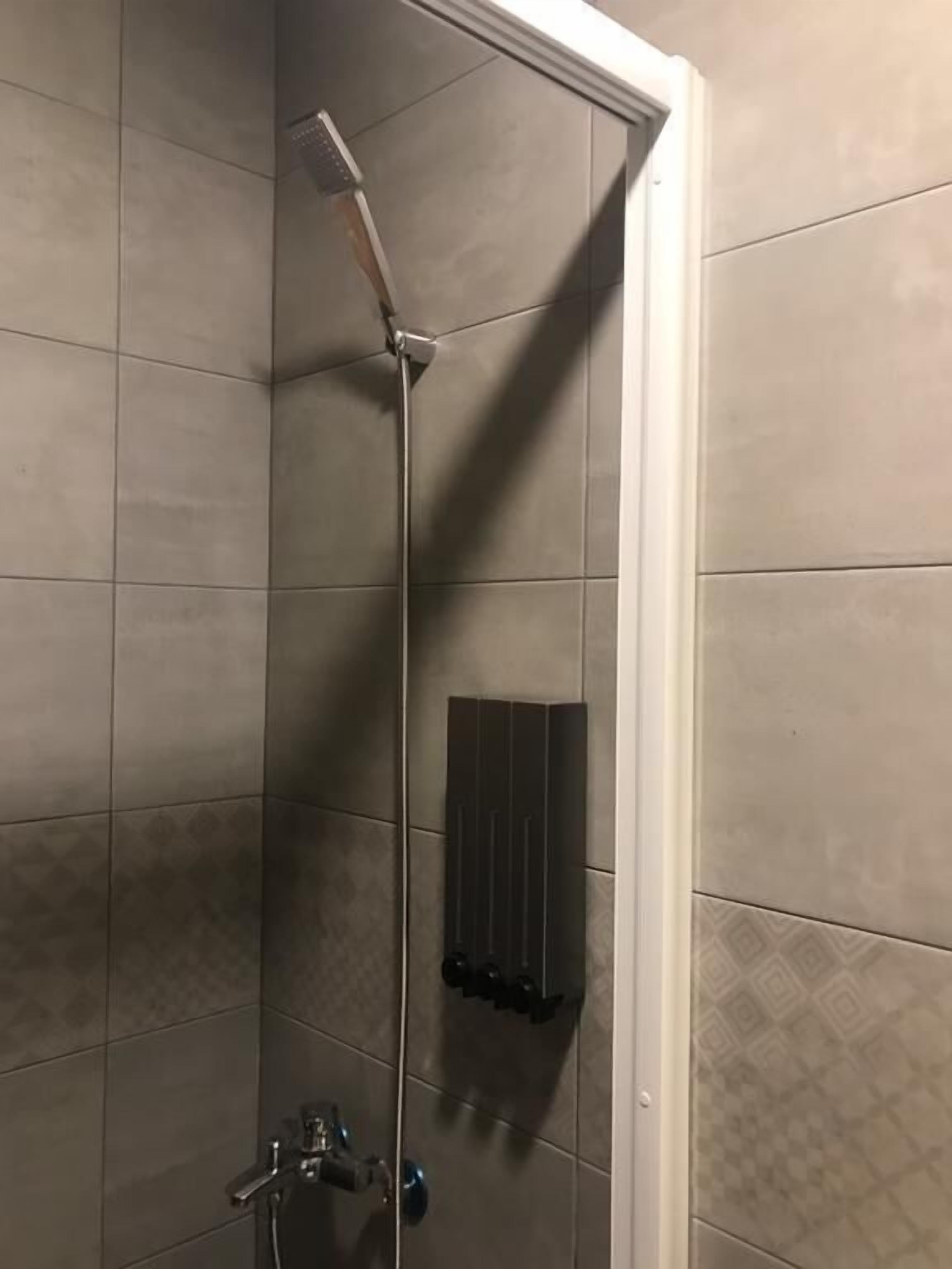 A shower with a handheld showerhead and a wall-mounted control panel.