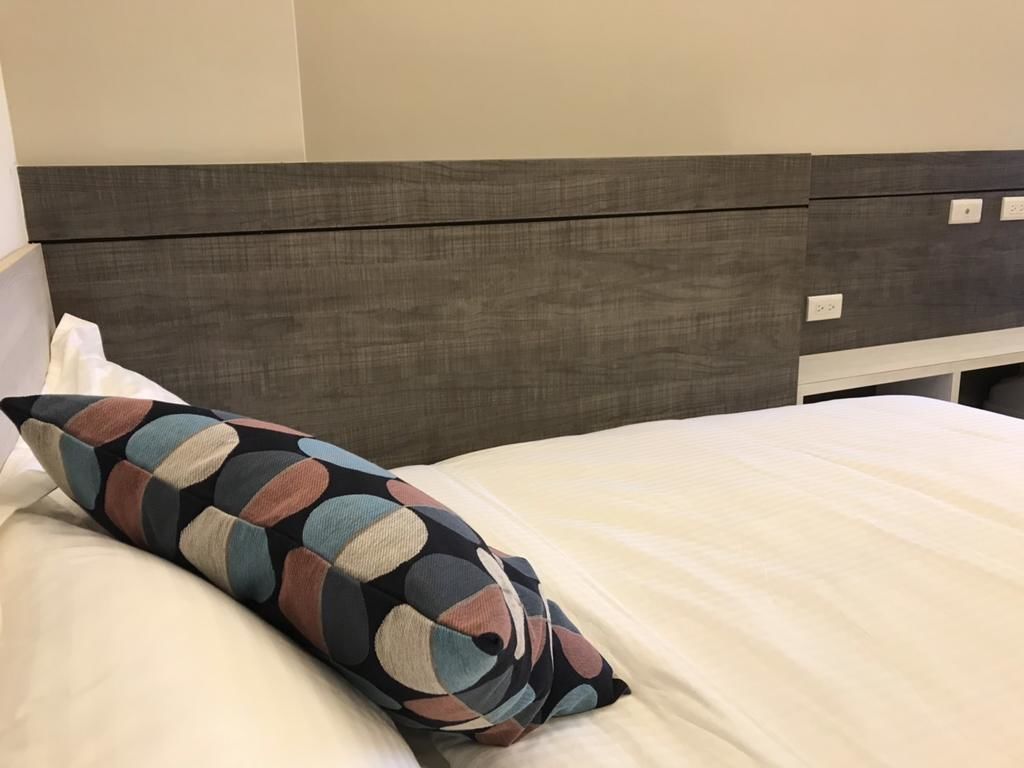 A bed with a multicolored pillow and a plain white sheet.