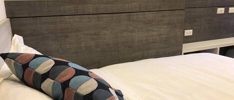 A bed with a multicolored pillow and a plain white sheet.