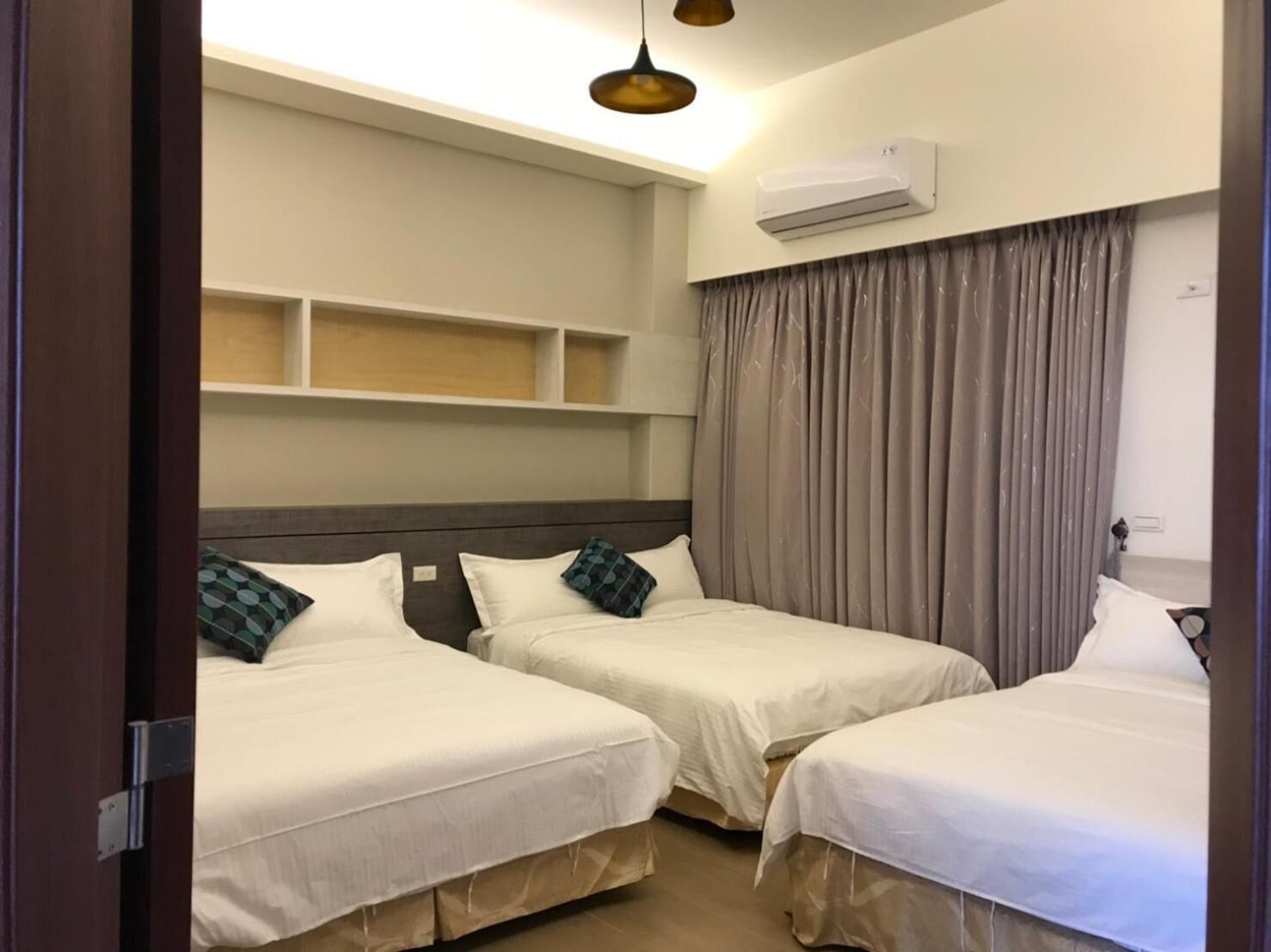 A hotel room with two single beds, a built-in shelf above the beds, an air conditioning unit on the wall, and a curtain on the window.