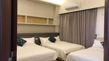 A hotel room with two single beds, a built-in shelf above the beds, an air conditioning unit on the wall, and a curtain on the window.