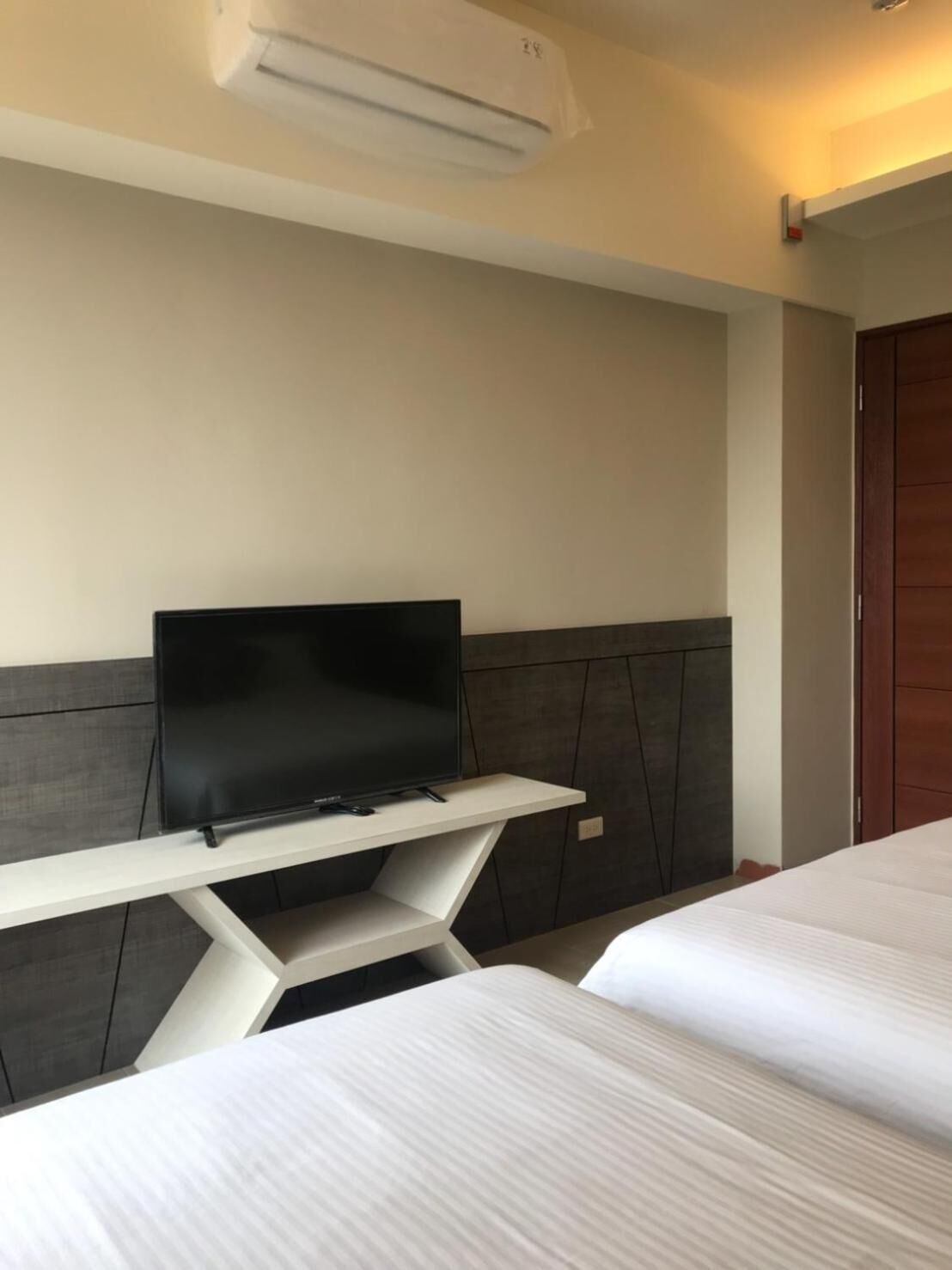 A hotel room with a bed, a TV on a white stand, and a wooden door.