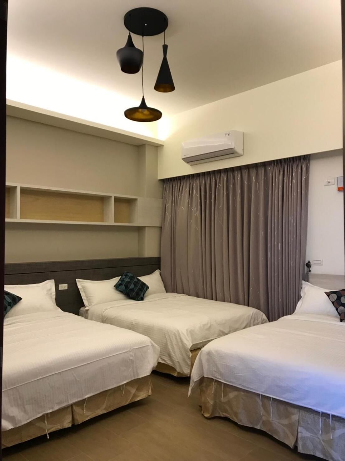 A hotel room with two beds, a ceiling light fixture, an air conditioning unit, and a window with curtains.
