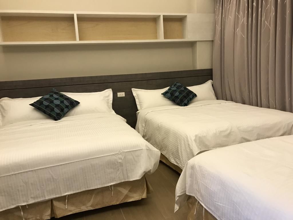 Two single beds with white bedding and dark headboards, a wooden floor, and a white shelf above the beds.