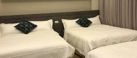 Two single beds with white bedding and dark headboards, a wooden floor, and a white shelf above the beds.