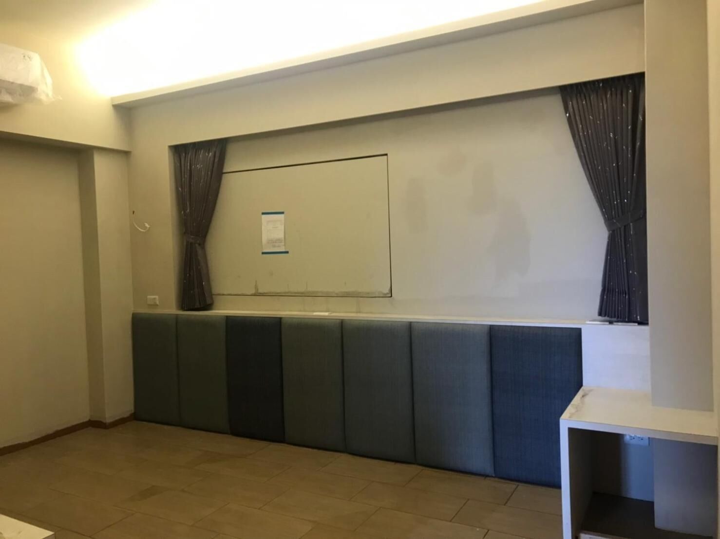 A hotel room with a large window, a whiteboard, and a seating area with cushioned benches.