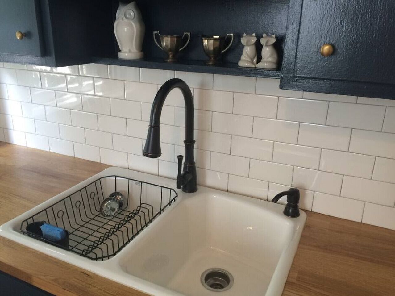 A kitchen sink with a black faucet, a dish rack, and a white tiled backsplash.