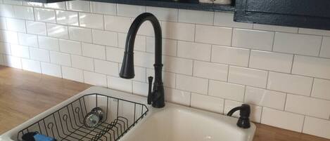 A kitchen sink with a black faucet, a dish rack, and a white tiled backsplash.