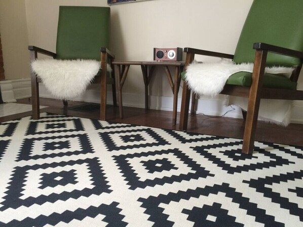 A room with two green chairs, a small table, and a patterned rug.