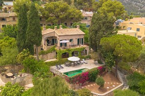 A Mediterranean-style villa with a pool, outdoor seating, and lush vegetation.