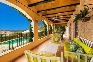 A covered outdoor area with a pool, seating, and a view of the landscape.
