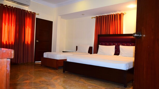 Habitación de hotel con dos camas individuales, cabecero de madera, piso con diseño de piedra y cortinas rojas.