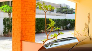 Un coche aparcado en un garaje con un pilar de ladrillo y vistas a una valla blanca y follaje exterior.
