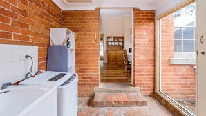 Cocina compacta con pared de ladrillo, lavadora y un pequeño comedor visible a través de una puerta abierta.