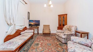Una habitación con cama, sillón, sofá, televisor, aparador y una alfombra estampada.