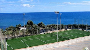Una cancha de tenis con vista despejada al océano y algunos árboles al fondo.