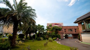 A building with a brick facade, a parking lot, and a grassy area with palm trees. - Beverly Commercial Motel (Taoyuan City)
