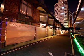 A street view at night with closed shop shutters, a brick building with a visible number 312, and a tall residential building in the background.