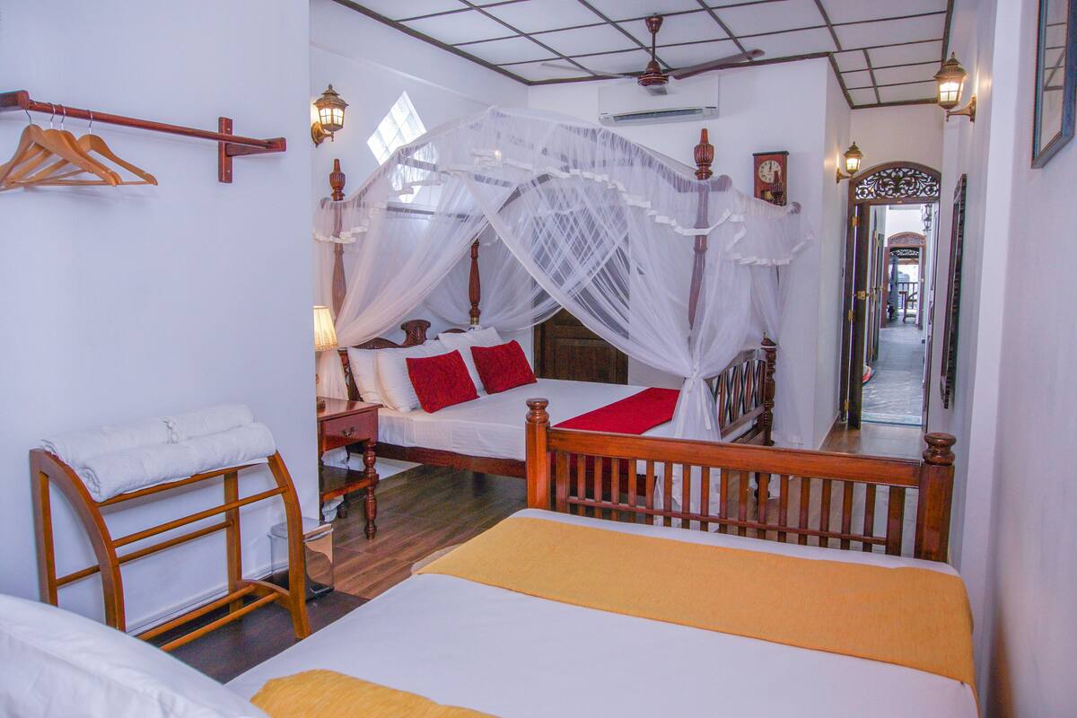 A bedroom with a canopy bed, a wooden headboard, a bedside table, and a hanging wooden rack.