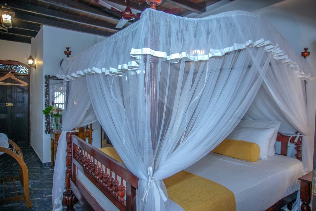 A bed with a canopy, a wooden headboard, and a yellow accent pillow.