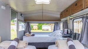 A compact RV bedroom with two beds, a small desk, and a window with curtains. - Leithfield Beach Holiday Park (Leithfield)