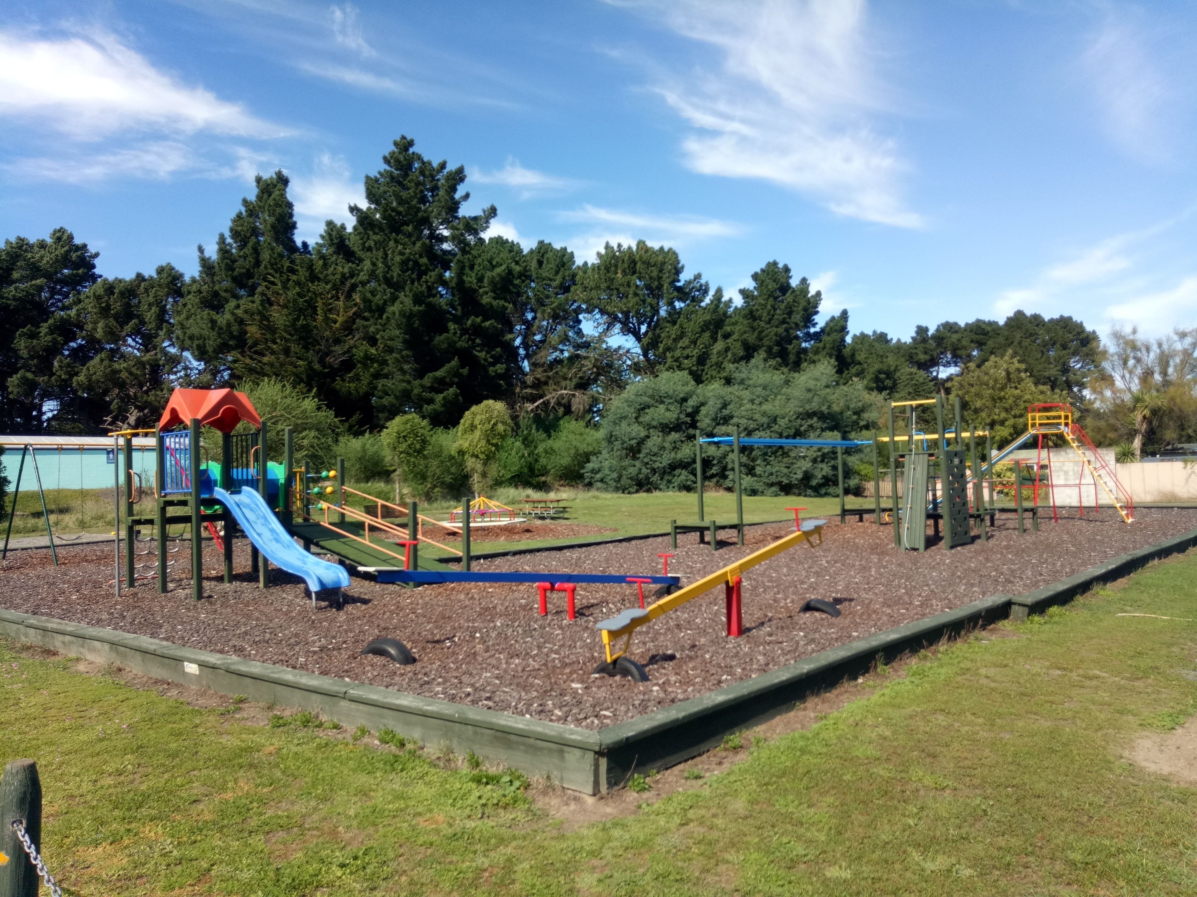A playground with various play structures, surrounded by trees and a clear sky.