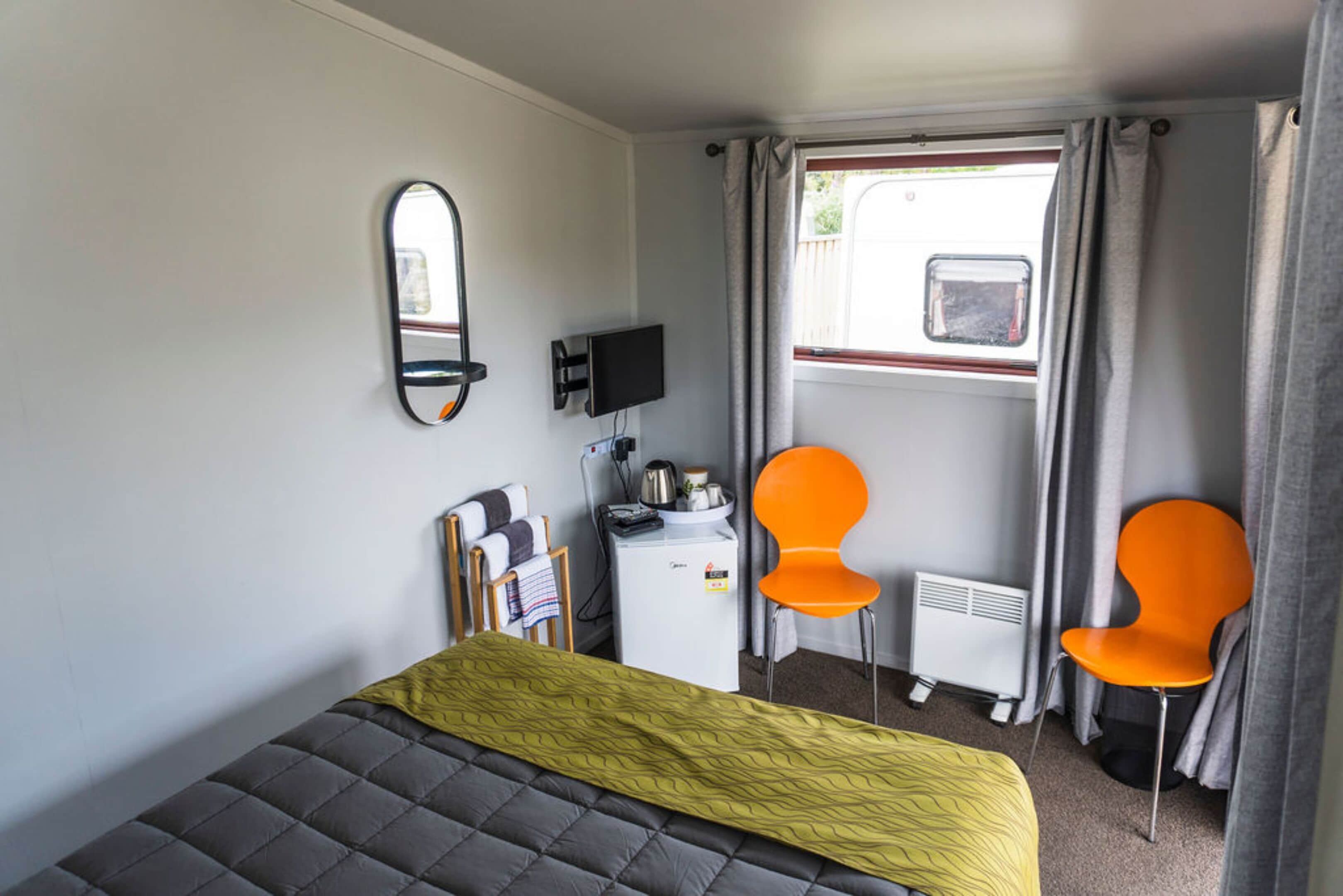 A compact room with a bed, a small desk, a television, two chairs, and a window with curtains.
