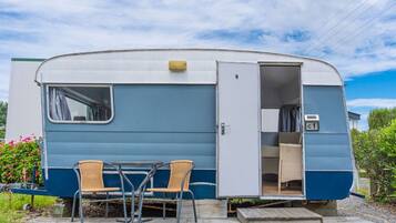 A blue and white recreational vehicle with an open door, two wicker chairs, and a small table outside.