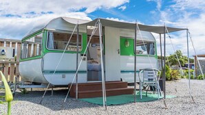 A vintage camper with a covered entrance, a small porch, and a step leading inside. - Leithfield Beach Holiday Park (Leithfield)