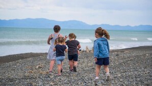 A group of children walking on a pebbled beach with a view of the sea and mountains in the background. - Leithfield Beach Holiday Park (Leithfield)