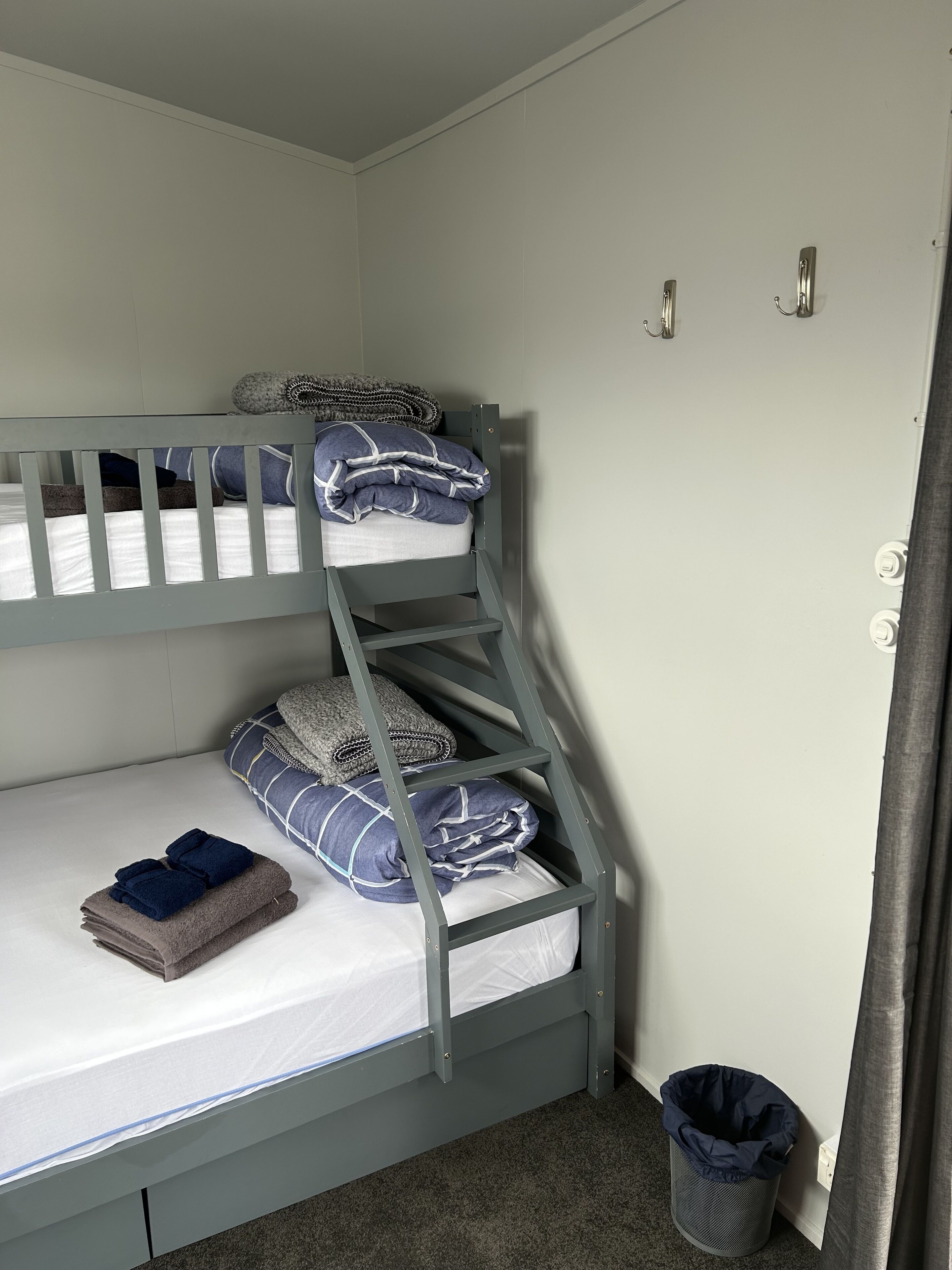 A bunk bed with two levels, a small trash bin, and a door with a handle.