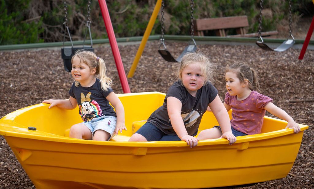 Three children in a yellow boat on a playground.