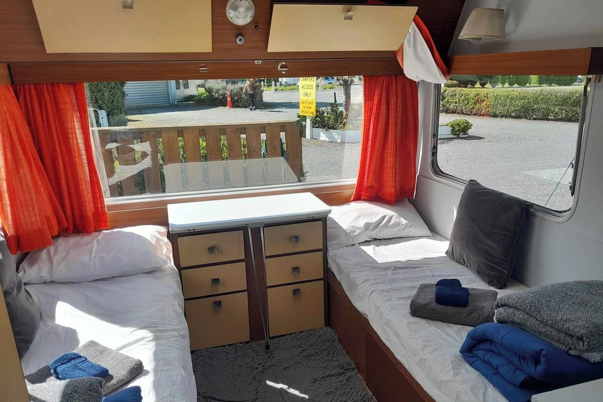 Interior compacto de RV com cama, escrivaninha pequena e janela com cortinas.