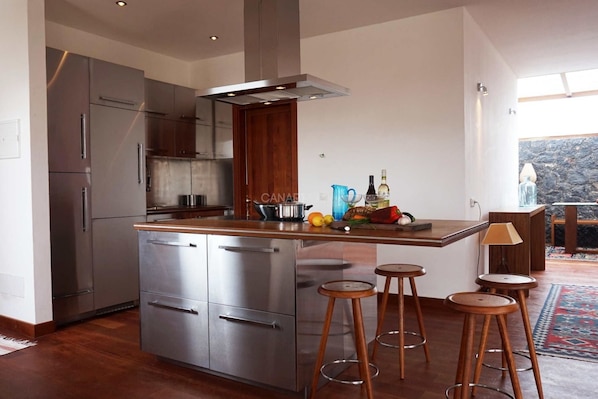 Eine moderne Küche mit Edelstahlgeräten, Holzhocker und Blick auf eine felsige Landschaft.