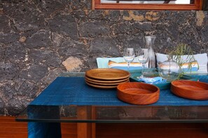 Ein Tisch mit gestapelten Holzschalen, einer Glasvase und einer Schüssel auf einer blauen Tischdecke vor einer Steinwand.
