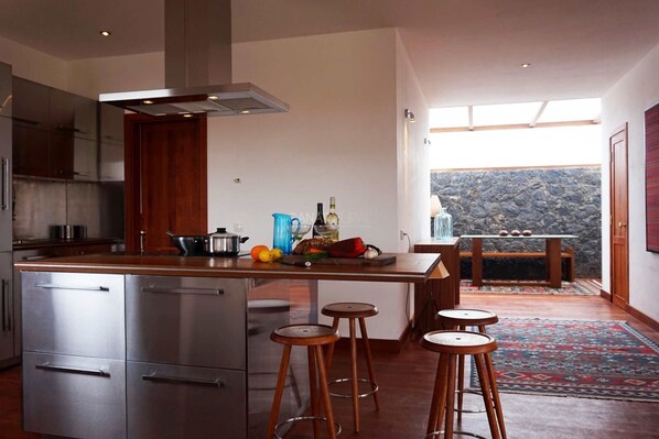 Une cuisine moderne dotée d’appareils électroménagers en acier inoxydable, d’un îlot central avec des tabourets et offrant une vue sur un paysage rocheux grâce à une grande fenêtre.